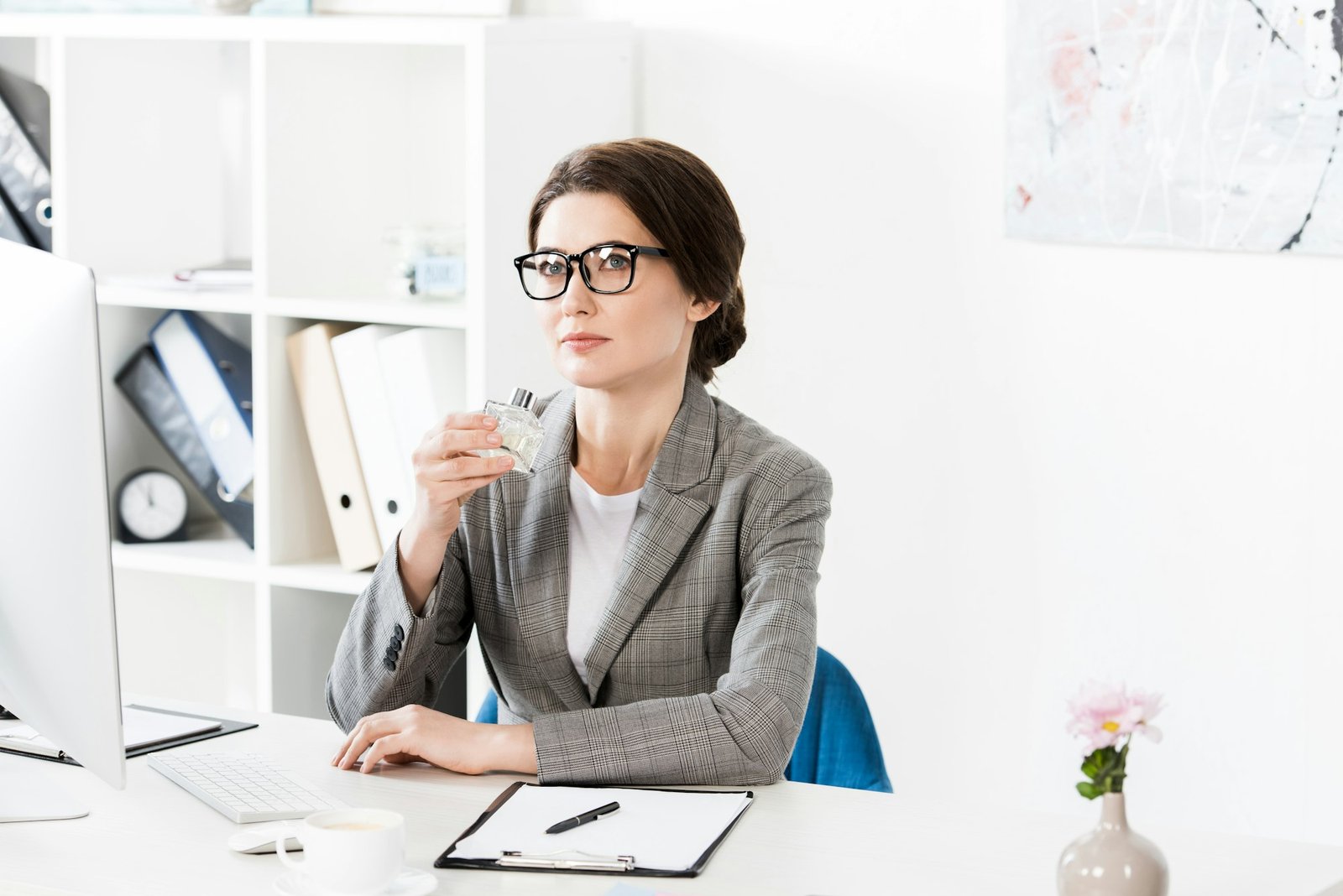 attractive businesswoman sniffing jar of perfume in office